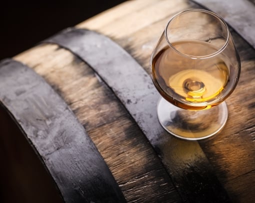 Snifter glass of brandy standing on an oak barrel in a cellar